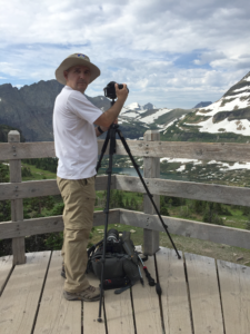 Eugeniu Grigorescu standing by a tripod and camera, photographing a mountain vista.